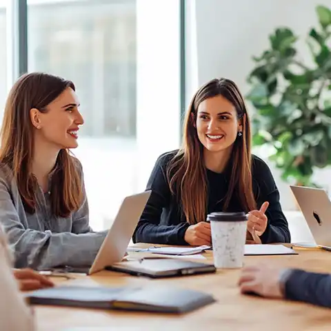 Fotografía de un grupo de jóvenes sonriendo, alrededor de una mesa llena de papeles en una oficina mientras conversan las estrategias digitales de marketing para sus productos y servicios.