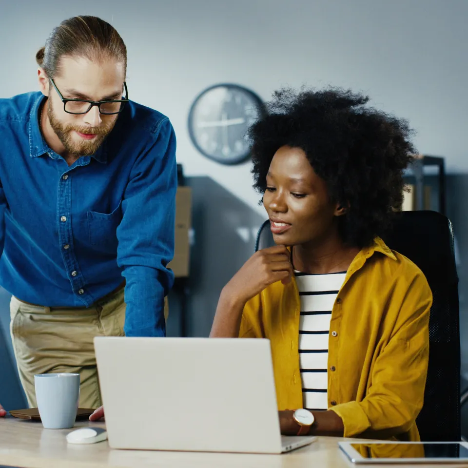 Fotografía de dos graduados del diplomado en gestión para la transformación digital conversando, sentados sobre una mesa, para decidir qué proyecto elegir para su organización. 
